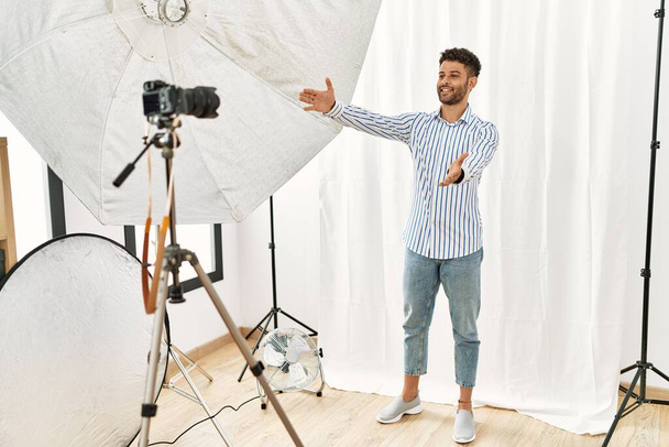 Arab fiatalember modellnek adja ki magát a fotóstúdióban, miközben a kamerát nézi, ahogy tárt karokkal mosolyog. vidám kifejezés, mely felöleli a boldogságot.  - Fotó, kép
