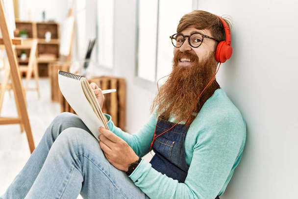 Jonge roodharige man luistert naar muziek en tekent in kunststudio - Foto, afbeelding