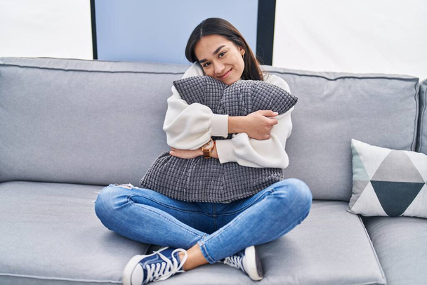 Fiatal spanyol nő ölelés párna ül kanapén otthon - Fotó, kép
