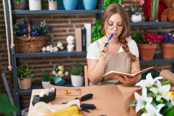 Giovane donna bionda fiorista pensando lettura notebook a fiorista - Foto, immagini