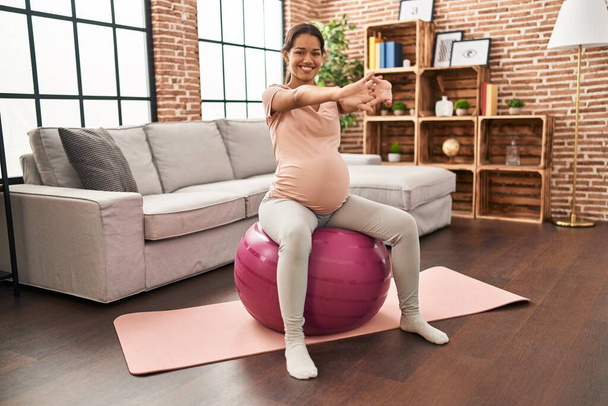 Young latin woman pregnant stretching using fit ball at home - Foto, Imagen