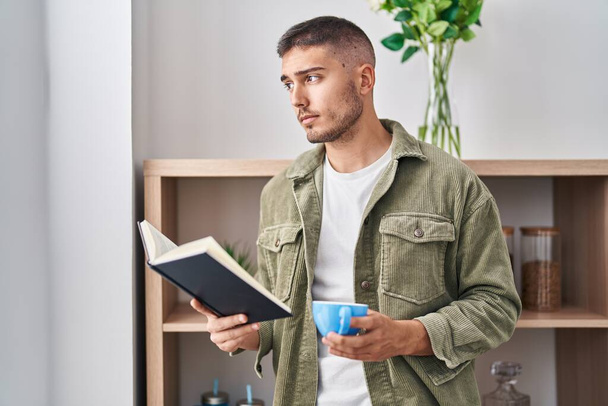 Young hispanic man reading book drinking coffee at home - Photo, Image