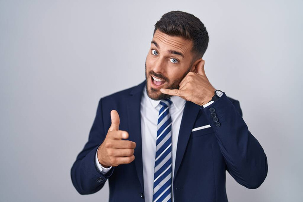 Handsome hispanic man wearing suit and tie smiling doing talking on the telephone gesture and pointing to you. call me.  - Photo, Image