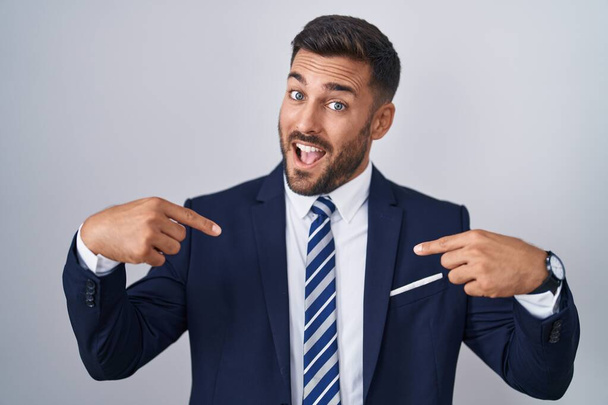 Hombre hispano guapo vistiendo traje y corbata mirando confiado con sonrisa en la cara, señalándose con los dedos orgullosos y felices.  - Foto, imagen