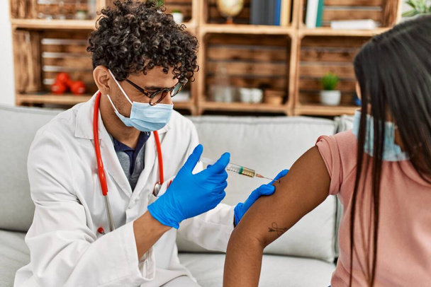 Młody lekarz wstrzykuje covid-19 szczepionkę przeciw koronawirusowi kobiecie siedzącej na kanapie w klinice. - Zdjęcie, obraz