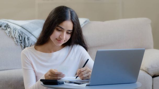 Young housewife arab middle eastern woman considers utilities uses calculator control domestic budget counts incomes outcomes bills writes notes documentation make paperwork account for spending costs - Photo, Image