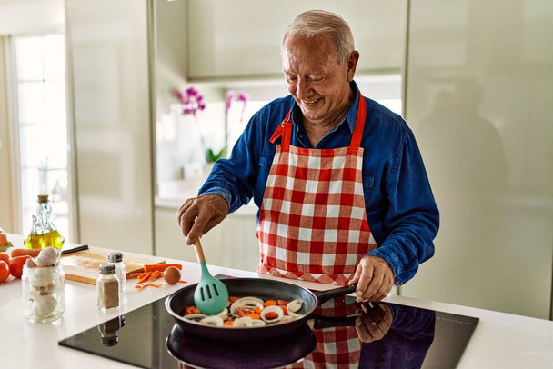Starší muž se usmívá sebevědomě vaření v kuchyni - Fotografie, Obrázek