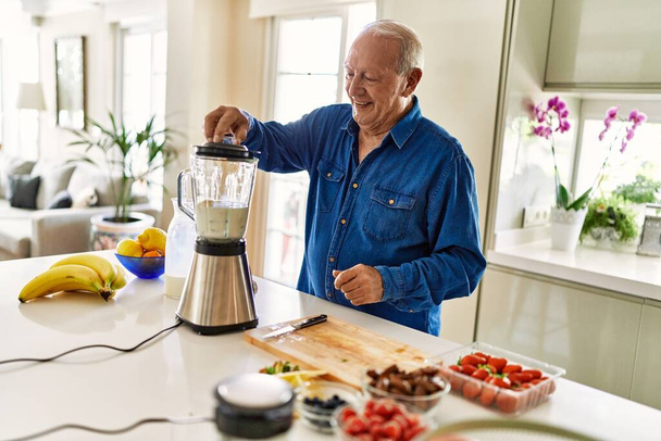 Senior man smiling confident shaking blender at kitchen - 写真・画像