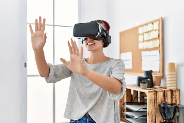 Young caucasian businesswoman smiling happy using virtual reality glasses at the office. - Photo, Image