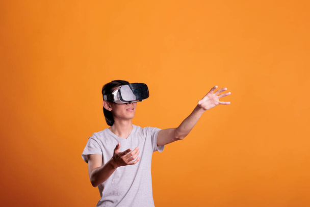 Man playing virtual reality games in vr goggles, exploring metaverse. Person wearing ar headset enjoying videogames, simulation experience, touching objects in cyberspace - Photo, Image