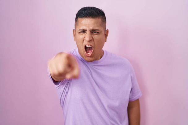 Joven hombre hispano de pie sobre fondo rosa señalando disgustado y frustrado a la cámara, enojado y furioso con usted  - Foto, Imagen