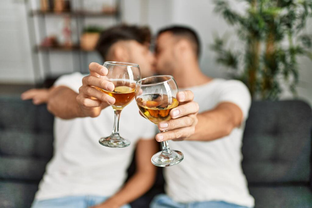 Two hispanic men couple kissing and toasting with glass of wine at home - Photo, Image