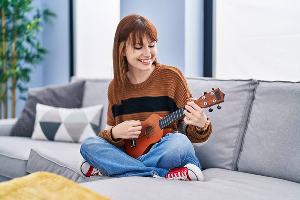 Mujer joven jugando ukelele sentado en el sofá en casa - Foto, imagen