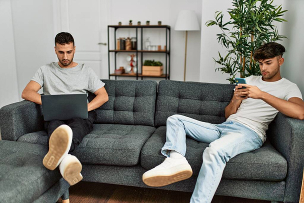 Two hispanic men couple using smartphone and laptop at home - Fotoğraf, Görsel