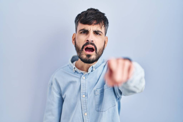 Nuori latinomies parta seisoo sininen tausta osoittaa tyytymätön ja turhautunut kameraan, vihainen ja raivoissaan sinulle  - Valokuva, kuva