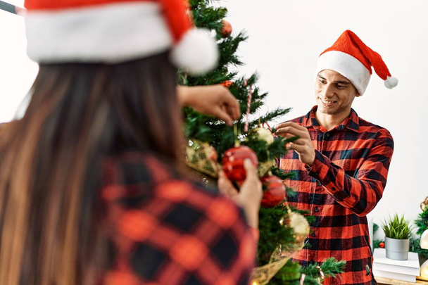 Νεαρό ζευγάρι Λατίνων χαμογελά ευτυχισμένη διακόσμηση χριστουγεννιάτικο δέντρο στο σπίτι. - Φωτογραφία, εικόνα
