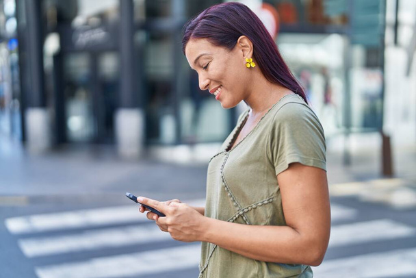 Νέα όμορφη ισπανόφωνη γυναίκα χαμογελά αυτοπεποίθηση χρησιμοποιώντας smartphone στο δρόμο - Φωτογραφία, εικόνα