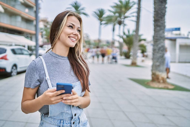 Молода біла дівчина посміхається щаслива, використовуючи смартфон у місті
. - Фото, зображення