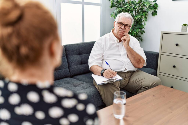 Старший психолог чоловік в консультаційному офісі з рукою на підборідді думає про питання, пенсійне вираження. усміхнений вдумливим обличчям. концепція сумніву
.  - Фото, зображення