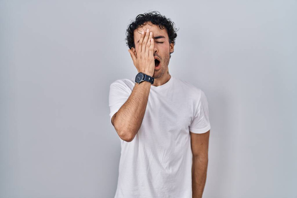 Латиноамериканець стоїть над ізольованим фоном, позіхаючи, закриваючи напівобличчя, очі та рот рукою. Біль завдає болю.  - Фото, зображення