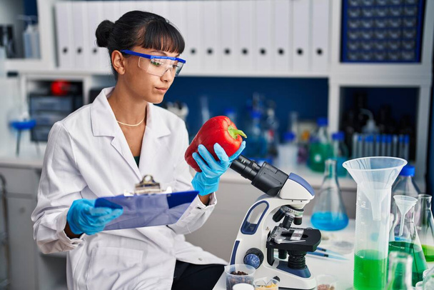 Молодая красивая латиноамериканка-ученый читает документ, держа перец в лаборатории - Фото, изображение