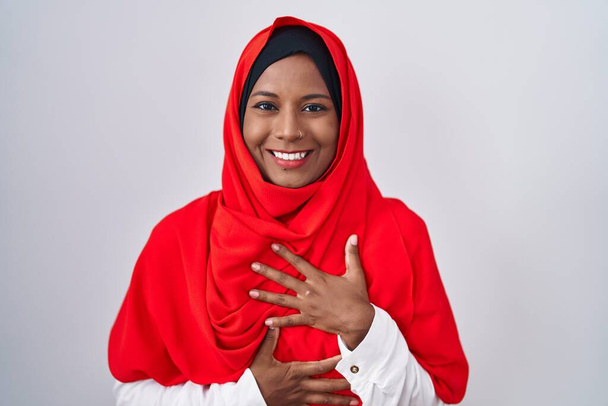 Jonge Arabische vrouw draagt traditionele islamitische hijab sjaal lachen en hard lachen hardop omdat grappige gekke grap met handen op het lichaam.  - Foto, afbeelding