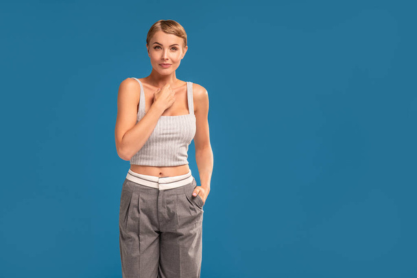 Fashion photo of blonde woman with short hairstyle looking at the camera, standing on blue studio background. A lot of copy space for your text. - Fotó, kép