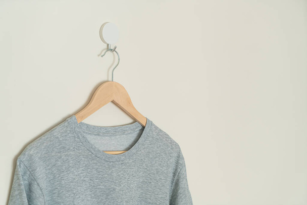 grey t-shirt hanging with wood hanger on wall - Foto, immagini