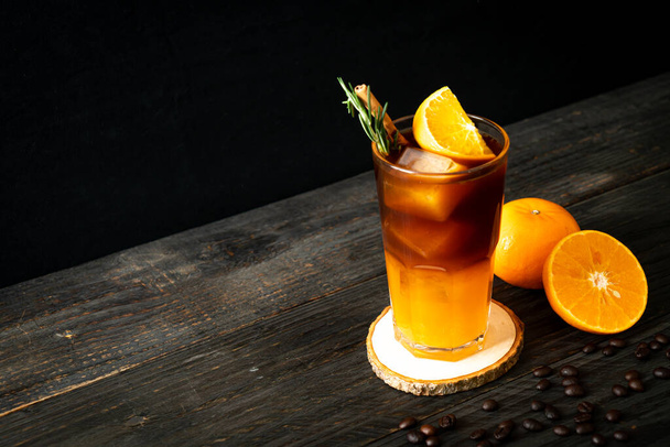 A glass of iced americano black coffee and layer of orange and lemon juice decorated with rosemary and cinnamon - Photo, Image