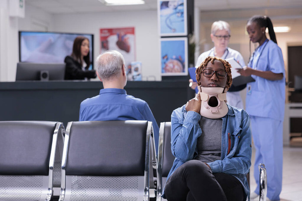 Paciente afro-americano com colar cervical sentado na sala de espera do hospital para participar do exame de check-up. Adulto jovem com lesão tendo consulta com especialista em centro de saúde. - Foto, Imagem