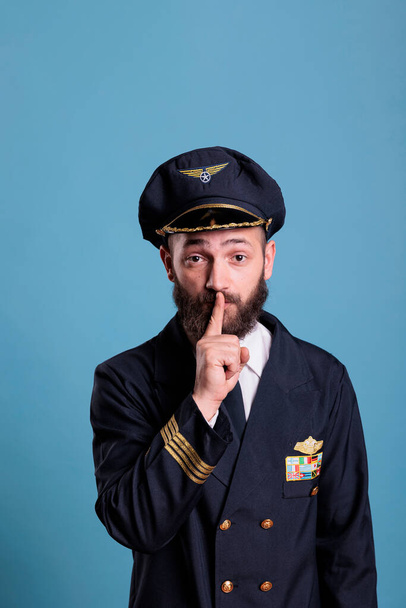 Πορτρέτο του καπετάνιου δείχνει σιωπηλή χειρονομία, κοιτάζοντας κάμερα με δείκτη στα χείλη. Αεροπορική ακαδημία αεροπλάνο pilor μπροστινή όψη, αεροπόρος της αεροπορίας κρατώντας μυστικό, ήσυχο, σημάδι σιωπής - Φωτογραφία, εικόνα