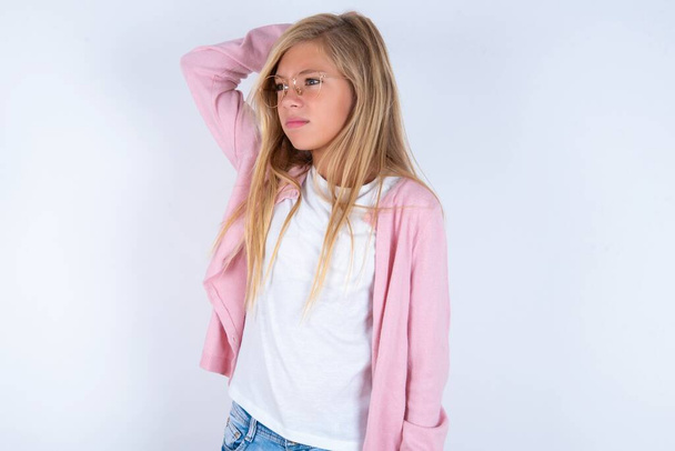 blond meisje dragen roze jas en bril over witte achtergrond denken - Foto, afbeelding