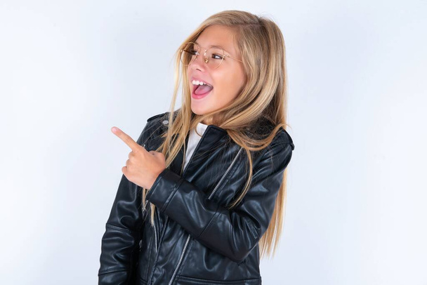 beautiful blonde little girl wearing biker jacket and glasses over white background demonstrating happiness close up portrait - Photo, Image