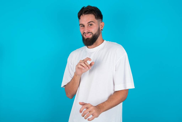 Ugh how disgusting! Displeased bearded caucasian man wearing white T-shirt over blue background , has dissatisfied facial expression as sees something abominable. - Photo, Image