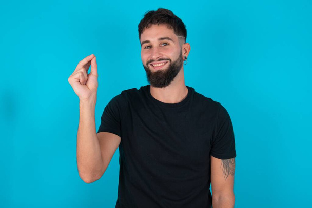 hispanique barbu homme portant noir T-shirt debout sur fond bleu pointant vers le haut avec la main montrant sept doigts geste en langue des signes chinoise Q.  - Photo, image