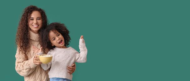 African-American woman and her little daughter with cup of hot chocolate on green background with space for text - Foto, Bild