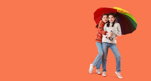 Portrait of cute twin girls with umbrella on orange background with space for text - Photo, Image