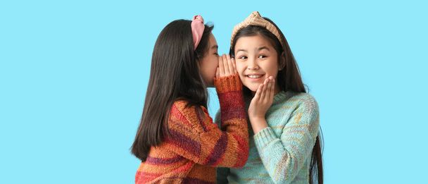 Cute little girl telling secrets to her sister on light blue background - Foto, Imagem