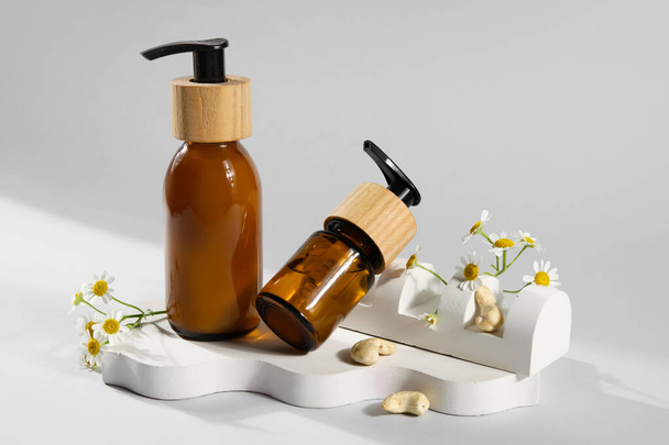 Beyaz arka planda doğal kozmetik ürünleri şişeleri ve papatya çiçekleri içeren kompozisyon - Fotoğraf, Görsel