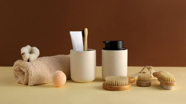 Bath accessories with cotton flower on table near brown wall - Foto, afbeelding