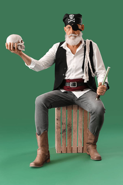 Viejo pirata con catalejo y cráneo humano sentado sobre fondo verde - Foto, imagen