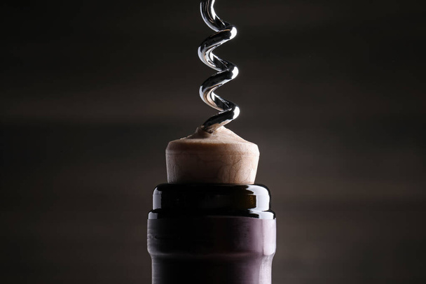 Opening wine bottle with corkscrew on dark background, closeup - Zdjęcie, obraz