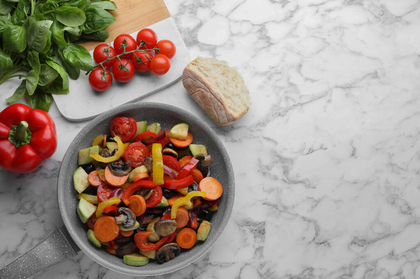 Mix of tasty vegetables in pan and ingredients on white marble table, flat lay. Space for text - Foto, Imagen