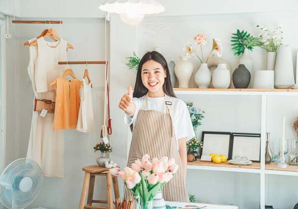 中小企業のオーナーは、顧客を歓迎し、オンラインで顧客を得るために彼らの小さな店で笑顔をポーズ。そして顧客がオンライン小売業者に注文した注文を確認してください-オンラインショッピング. - 写真・画像