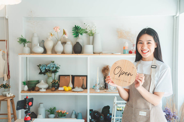 Smiling online small business owner holding a sign saying "Open" and happily working at a courier business offering orders and products to customers.Online retailer - online shopping. - Foto, Imagen