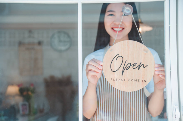 Smiling online small business owner holding a sign saying "Open" and happily working at a courier business offering orders and products to customers.Online retailer - online shopping. - Fotó, kép