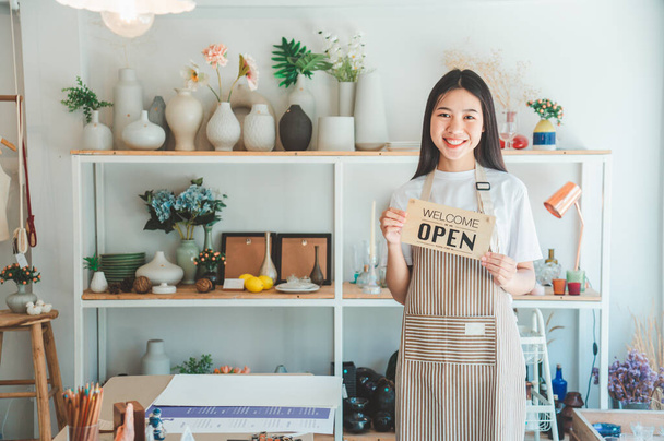 Smiling online small business owner holding a sign saying "Open" and happily working at a courier business offering orders and products to customers.Online retailer - online shopping. - Foto, Imagen