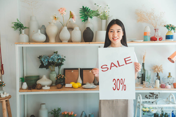 Smiling online small business owner holding a sign saying "sale 30%" and happily working at a courier business offering orders and products to customers.Online retailer - online shopping. - Foto, imagen
