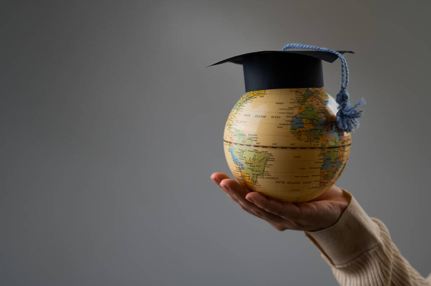 Woman holding a globe wearing a graduation cap - Фото, изображение