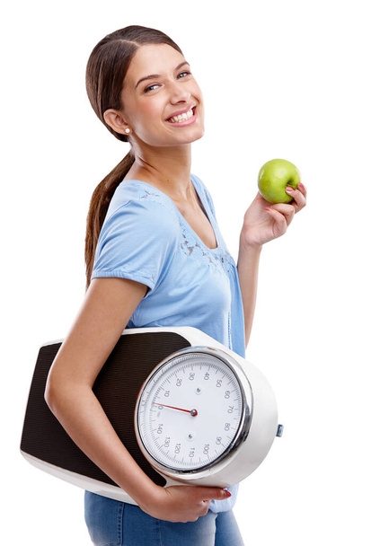 Eat well and exercise, thats the key. Portrait of an attractive young woman holding an apple and a scale against a white background - Foto, Bild